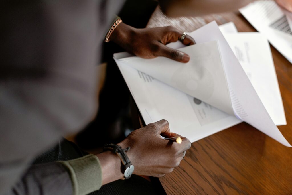African American adult revising papers with a pencil at a desk, focus on hands and documents.
